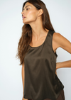 A woman wearing a dark brown satin sleeveless tank top, shown from a side profile against a light gray studio background.