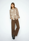 A woman modeling a beige and brown vertically striped long-sleeve blouse with white floral embroidery, paired with brown wide-leg pants and black pointed shoes, against a plain white studio background.