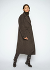 A model wearing a long, dark brown double-breasted wool coat over a black turtleneck, paired with black leather boots, photographed against a light gray studio background.