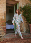 A woman wearing a matching long-sleeve pajama set with a green, pink, and white floral pattern walks barefoot out of a rustic stone doorway onto a brick patio.