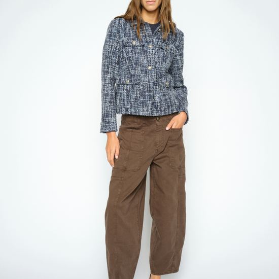 A woman modeling a blue and white textured tweed jacket paired with brown wide-leg cropped pants and dark brown pointed-toe heels, set against a plain light gray studio background.