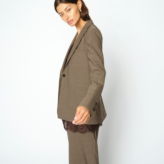 A woman modeling a matching taupe brown two-piece suit, featuring a structured blazer and wide-leg trousers, posed against a light gray studio background.