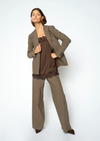 A woman modeling a taupe brown two-piece pantsuit consisting of a blazer and matching trousers, layered over a dark brown lace-trimmed camisole, against a light gray studio background.