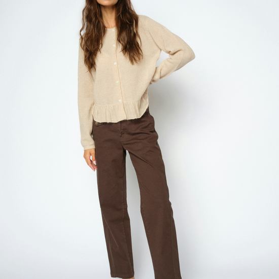 A woman modeling a beige knit cardigan sweater and brown straight-leg trousers, paired with beige pointed-toe heels, against a light gray studio background.