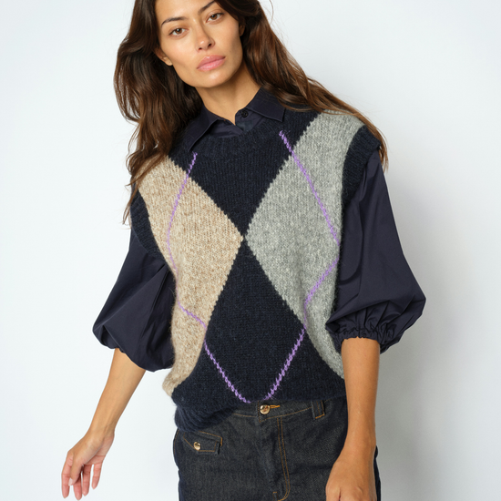 Woman wearing Blue, grey and beige Argyle vest with a blouse underneath
