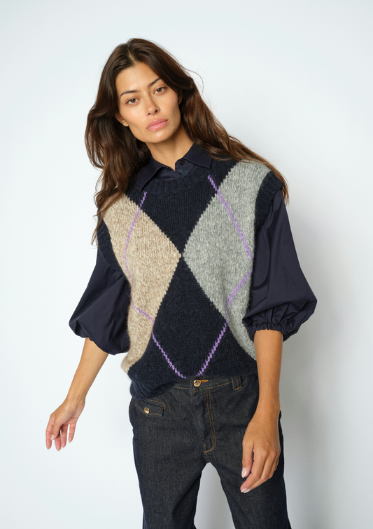 Woman wearing Blue, grey and beige Argyle vest with a blouse underneath