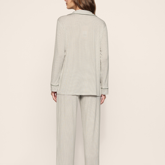A woman shown from the back wearing a light sage green and white micro-check patterned pajama set, consisting of a long-sleeve top and matching wide-leg pants, against a plain beige studio background.