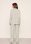 A woman shown from the back wearing a light sage green and white micro-check patterned pajama set, consisting of a long-sleeve top and matching wide-leg pants, against a plain beige studio background.