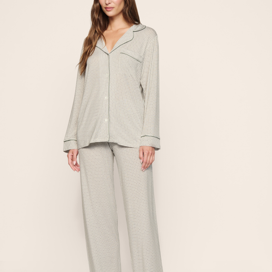 A woman modeling a light sage green waffle-knit pajama set with a long-sleeve button-up top and matching wide-leg pants, standing against a plain beige studio background.