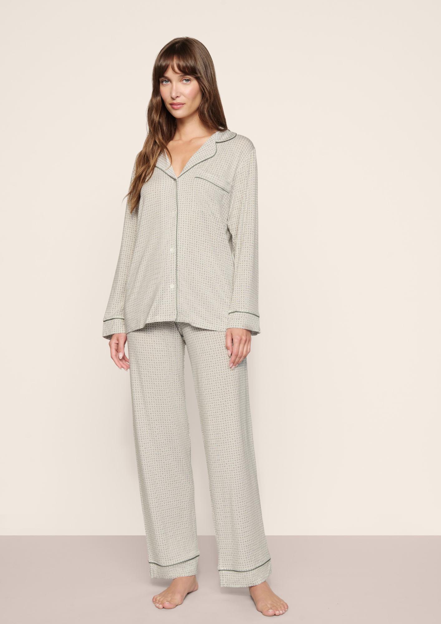 A woman modeling a light sage green waffle-knit pajama set with a long-sleeve button-up top and matching wide-leg pants, standing against a plain beige studio background.