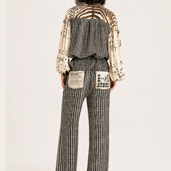 A model viewed from the back wearing a patterned jumpsuit with a cream and black-and-white houndstooth pattern, wide-leg trousers, and a back design featuring a zebra print and patch pockets.