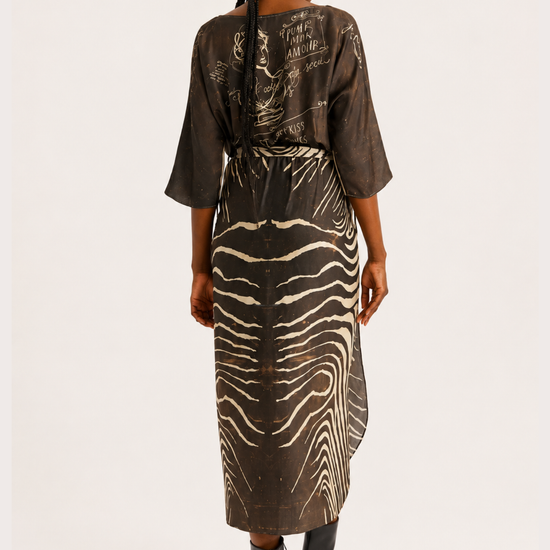 A woman viewed from the back wearing a sheer brown kimono-style dress with a zebra-stripe pattern and black ankle boots, photographed against a plain light background.