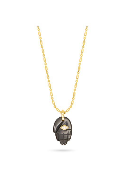 black hand pendant on a gold chain, with a gemstone in the centre, as a flat lay image on a plain white background 