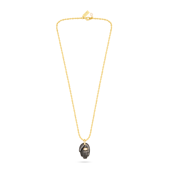 A delicate gold chain necklace featuring a small, dark metallic pendant with a textured, hammered finish, displayed against a solid white background.