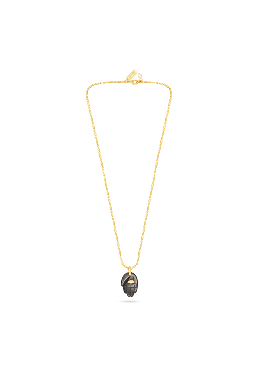 A delicate gold chain necklace featuring a small, dark metallic pendant with a textured, hammered finish, displayed against a solid white background.