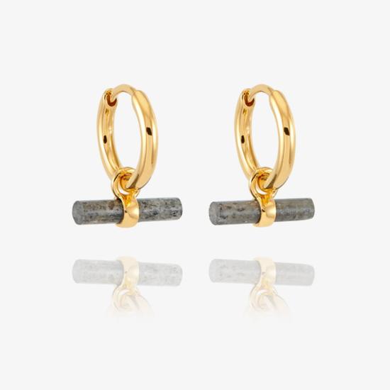 A pair of gold huggie hoop earrings with a small horizontal gray stone bar dangling from the bottom, shown on a clean white background with a soft reflection below.