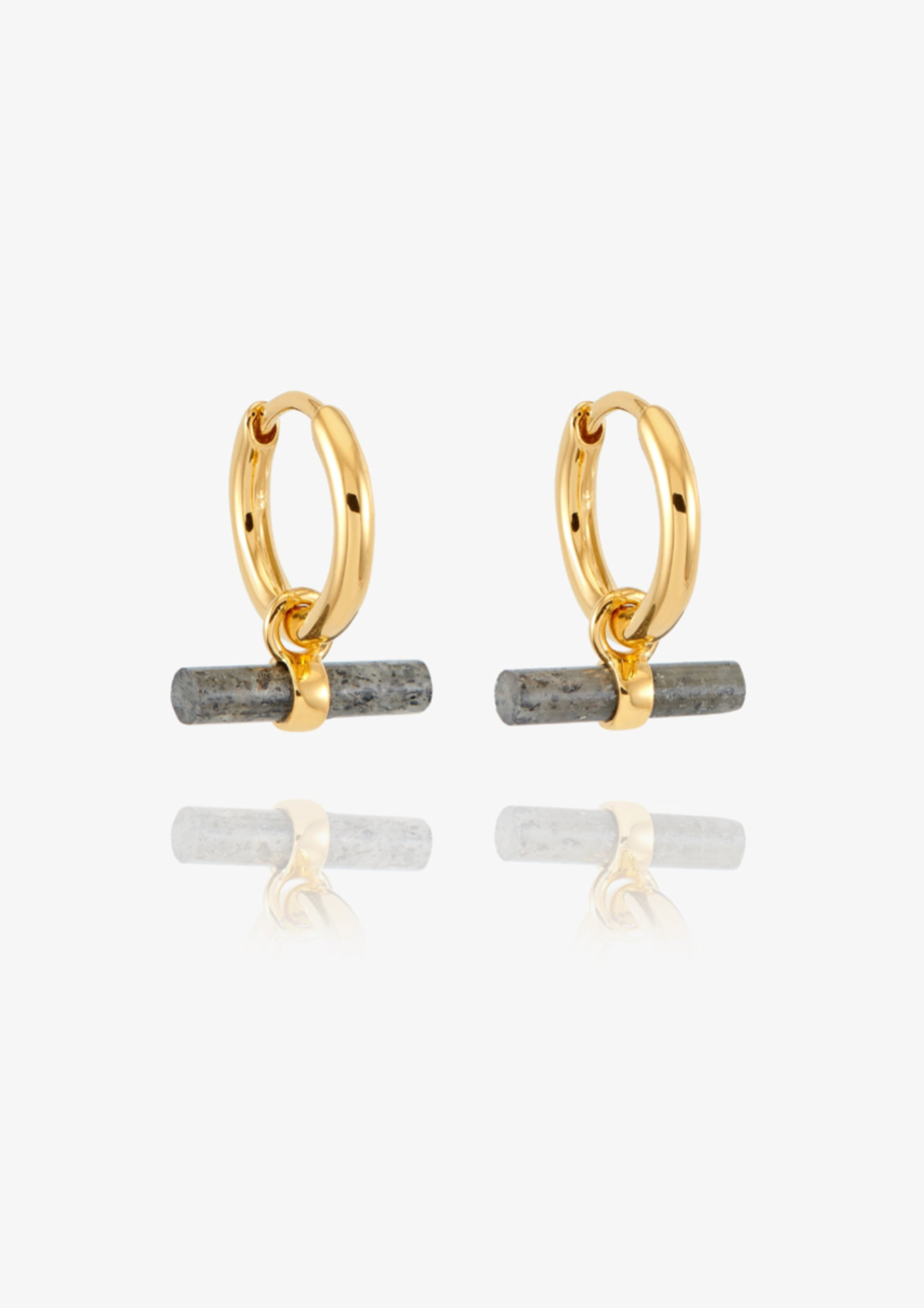 A pair of gold huggie hoop earrings with a small horizontal gray stone bar dangling from the bottom, shown on a clean white background with a soft reflection below.