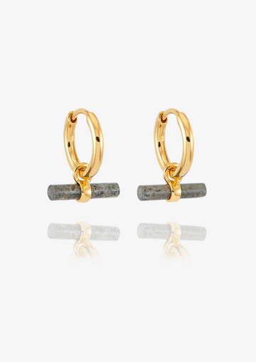 A pair of gold huggie hoop earrings with a small horizontal gray stone bar dangling from the bottom, shown on a clean white background with a soft reflection below.