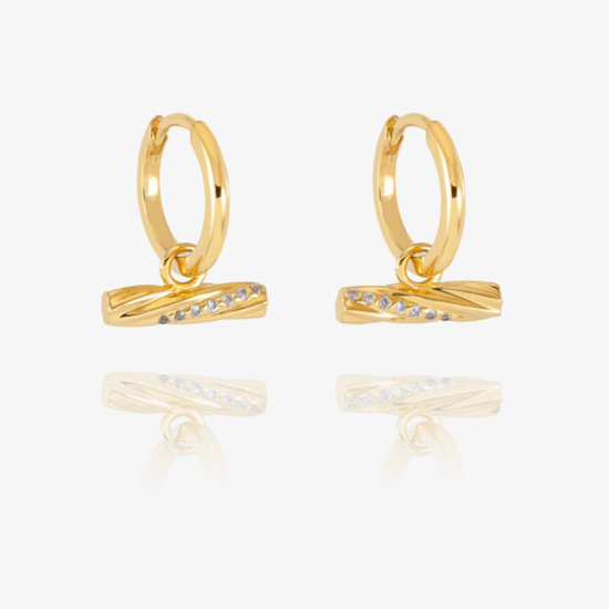 A pair of gold huggie hoop earrings with a twisted bar element set with small clear stones, displayed on a clean white background with a soft reflection below.