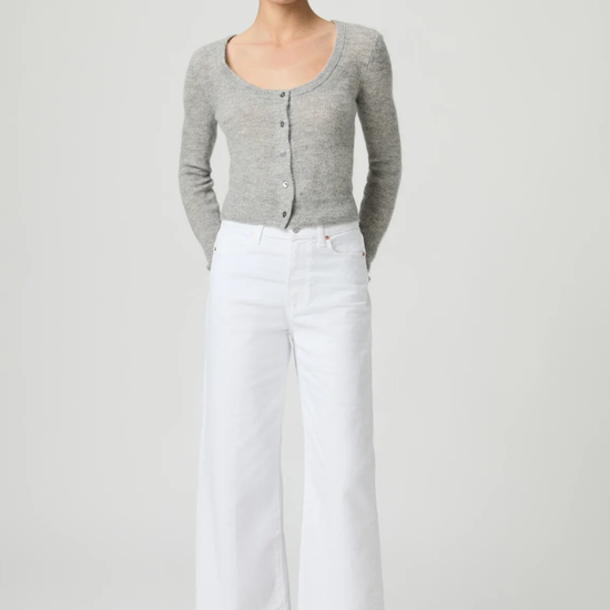 Woman wearing a gray cardigan and white paige jeans on a plain background