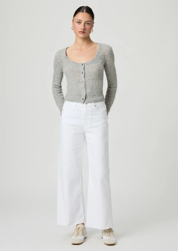 Woman wearing a gray cardigan and white paige jeans on a plain background