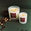 Two Connock candles on a dark green surface with pine cones and nuts.