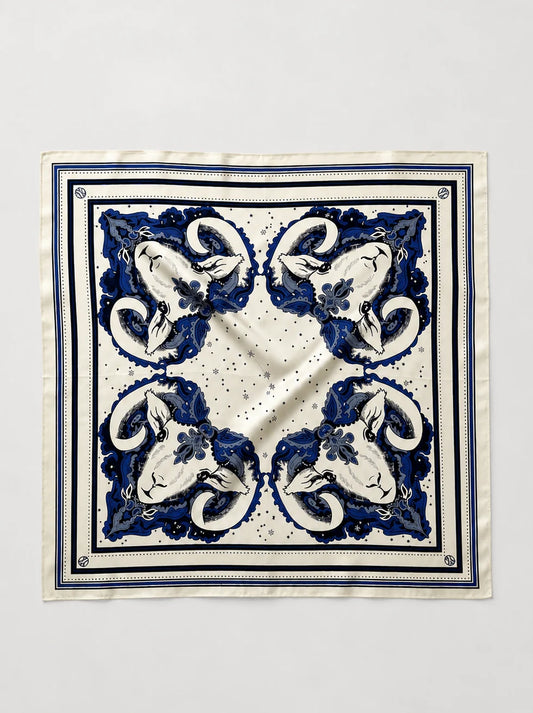 A square silk scarf with a classic blue and white baroque-style floral pattern, laid flat against a light gray background.