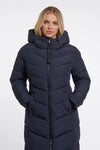 A woman wearing a long, dark navy puffer coat with a hood and front zipper, photographed against a plain light gray studio background.