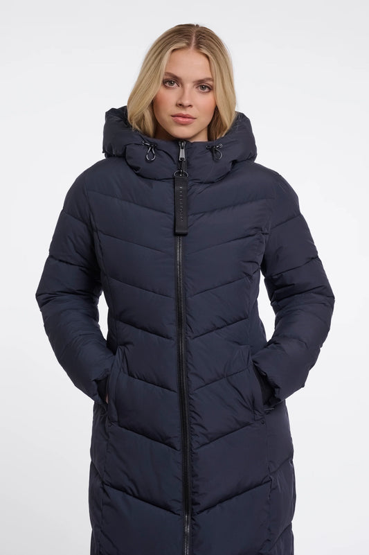 A woman wearing a long, dark navy puffer coat with a hood and front zipper, photographed against a plain light gray studio background.