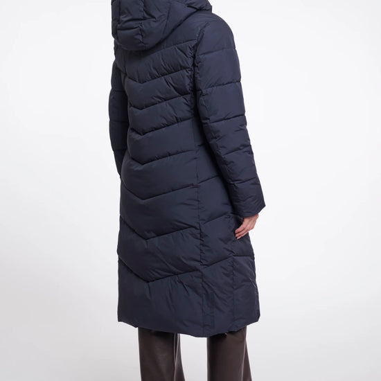 Person wearing a long navy blue puffer coat on a white background