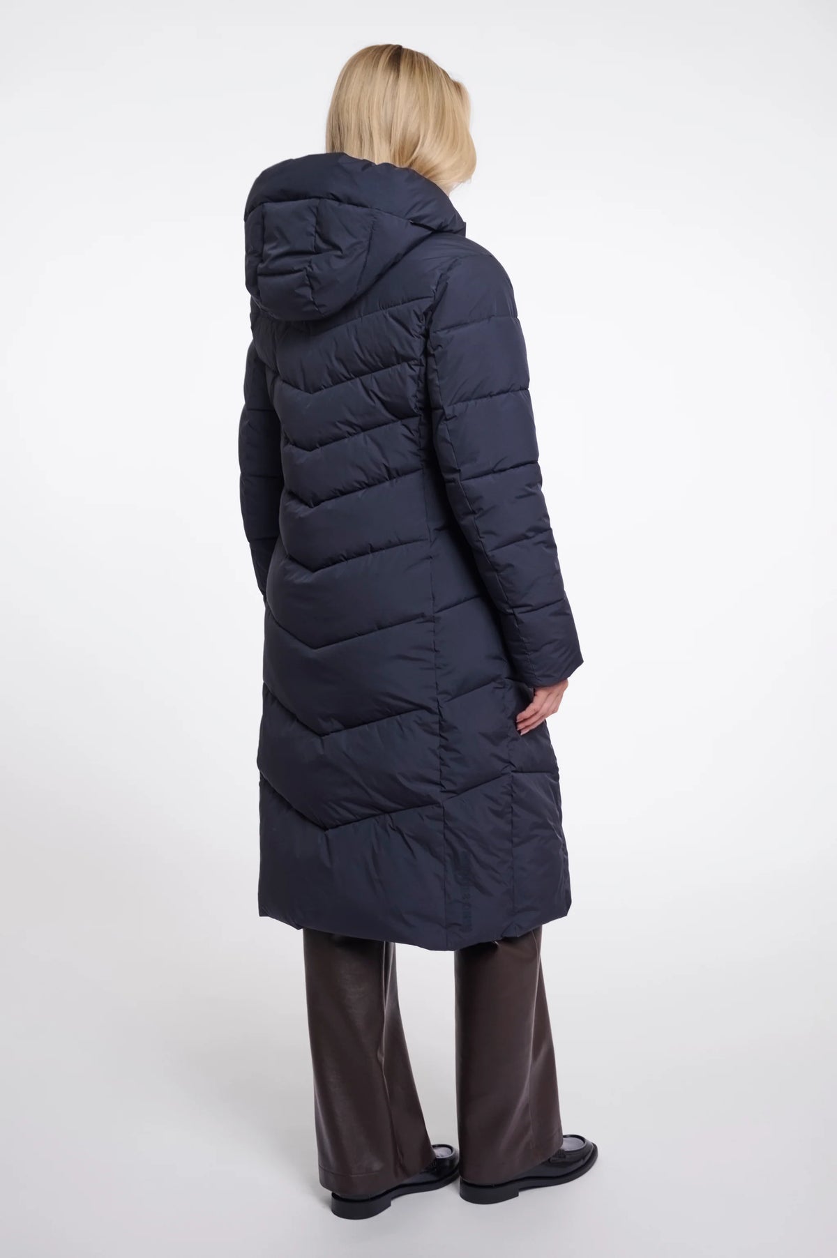 Person wearing a long navy blue puffer coat on a white background