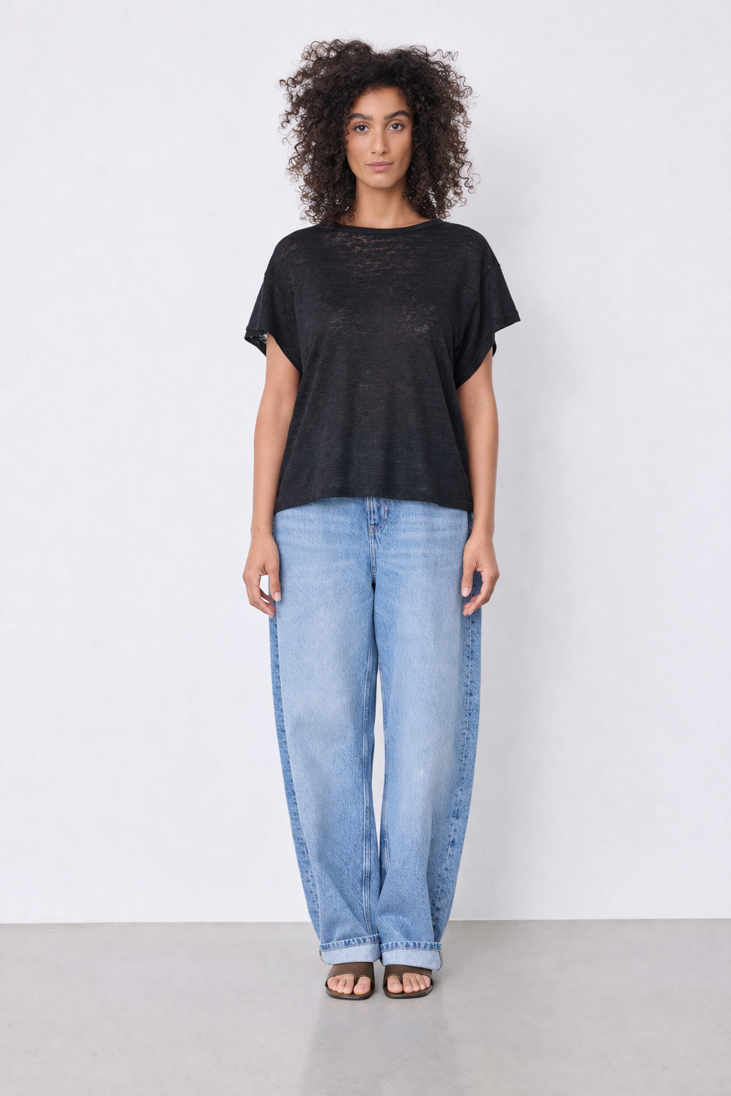 Model wearing black top and blue jeans on plain background 
