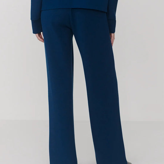 Rear view of a person wearing navy blue wide-leg trousers with a matching navy top, photographed against a light gray studio background.