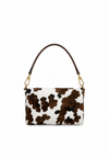 A small shoulder bag with a brown and black cow print pattern on a white background, featuring a dark brown leather shoulder strap and gold-tone hardware.