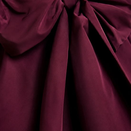 A close-up of a deep burgundy satin fabric with a large bow and gathered draping folds.