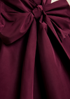 A close-up of a deep burgundy satin fabric with a large bow and gathered draping folds.