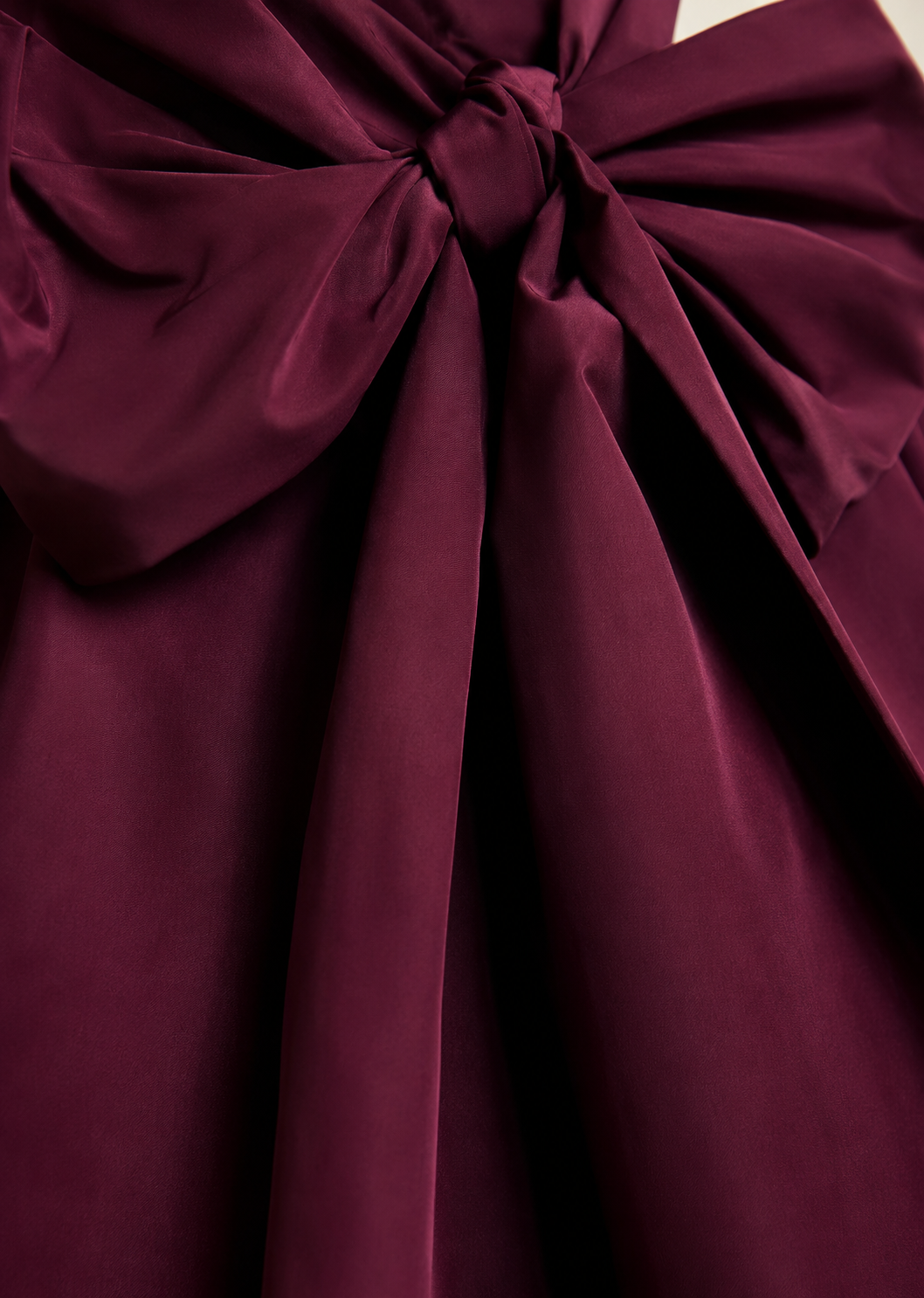 A close-up of a deep burgundy satin fabric with a large bow and gathered draping folds.