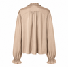 A beige long-sleeve blouse shown from the back, featuring a ruffled high neckline, gathered shoulder seams, and elasticized ruffled cuffs, displayed on a clean white background.