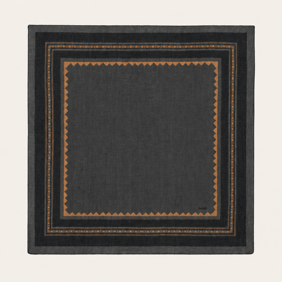 A square dark charcoal gray scarf with a geometric border pattern in brown and gold, displayed flat against a light cream background.