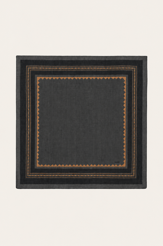 A square dark charcoal gray scarf with a geometric border pattern in brown and gold, displayed flat against a light cream background.