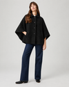 model wearing black cape style coat with blue denim jeans and black boots on a plain white background