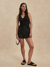 Woman wearing a black sleeveless top and shorts against a beige background