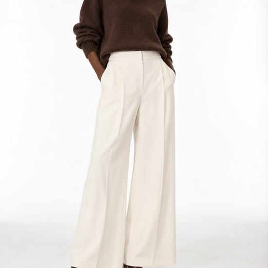 A model wearing a brown knit sweater and high-waisted off-white wide-leg trousers, paired with dark brown leather shoes, against a plain white studio background.