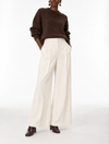 A model wearing a brown knit sweater and high-waisted off-white wide-leg trousers, paired with dark brown leather shoes, against a plain white studio background.