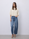 A woman modeling a cream short-sleeve knit top and wide-leg blue jeans with snakeskin heels, standing against a light gray studio background.