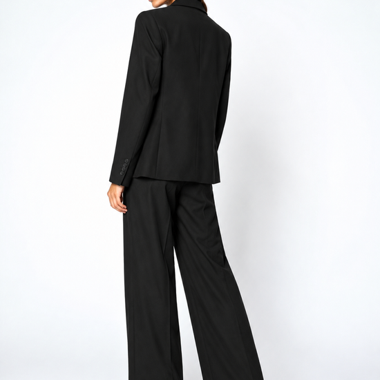 A model wearing a black tailored blazer and matching wide-leg trousers, shown from a three-quarters back view against a plain white studio background.