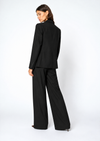 A model wearing a black tailored blazer and matching wide-leg trousers, shown from a three-quarters back view against a plain white studio background.