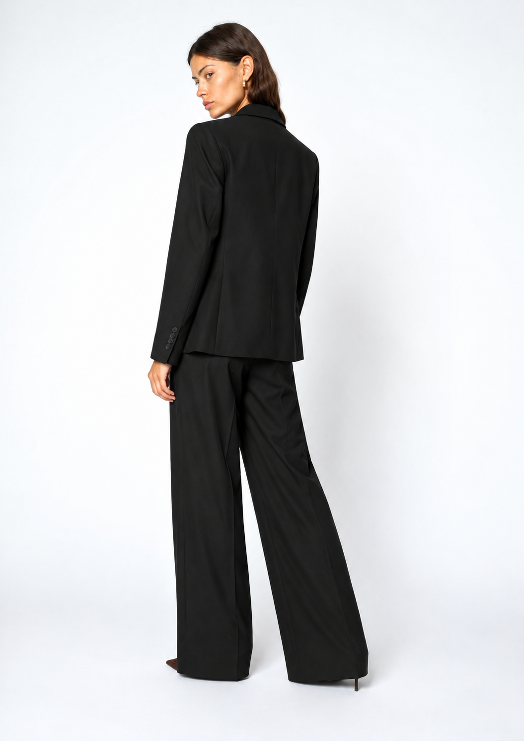 A model wearing a black tailored blazer and matching wide-leg trousers, shown from a three-quarters back view against a plain white studio background.