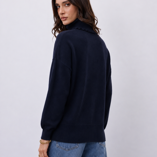 A woman wearing a dark navy blue ribbed knit sweater with a high mock neck, shown from a three-quarter back view against a light gray studio background.