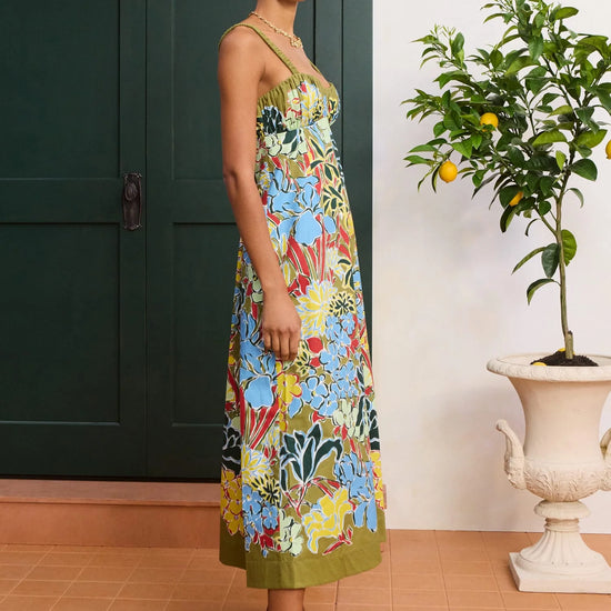 Woman wearing a colorful floral dress standing in a room with a plant and green door from Alemais
